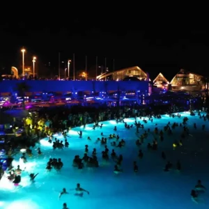 Nighttime aerial view of a packed pool party at Cafe Del Mar Malta, with lights and music filling the air.