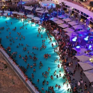 Aerial view of a packed pool party at Cafe Del Mar Malta, with lights reflecting off the water and people dancing.