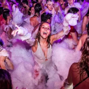 Group of dancers enjoying the foam-covered dance floor with vibrant lights at the Flirt Foam Party, Aria Complex, Malta.