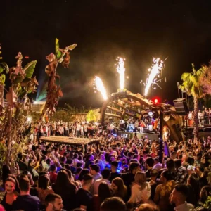 A vibrant outdoor party at Gianpula Malta’s G7 Fridays, with palm trees and flame effects.