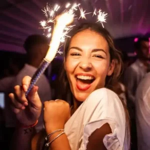 A smiling young woman holding sparklers at a VIP table during the White Party at Hugo Hotel Malta, adding excitement to the evening.
