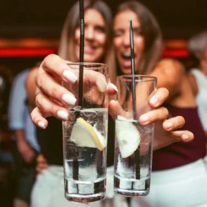 Two women in white celebrating at the White Party at Twenty Two Malta, toasting with close-up on their cocktails.