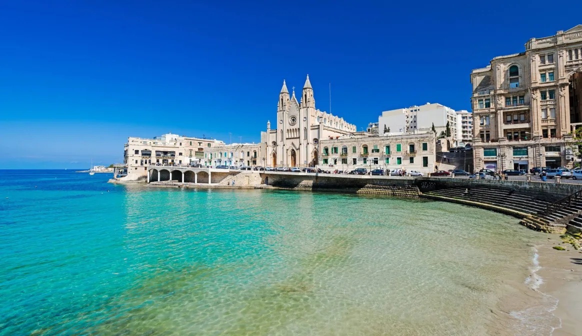 Balluta Bay beach Malta – piccola cala sabbiosa a St Julian's con la chiesa Art Nouveau sullo sfondo
