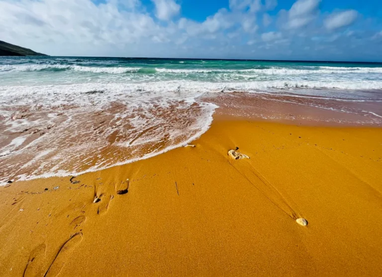 Close-up of Ramla Bay's famous red-orange sand with turquoise waves washing ashore in Gozo