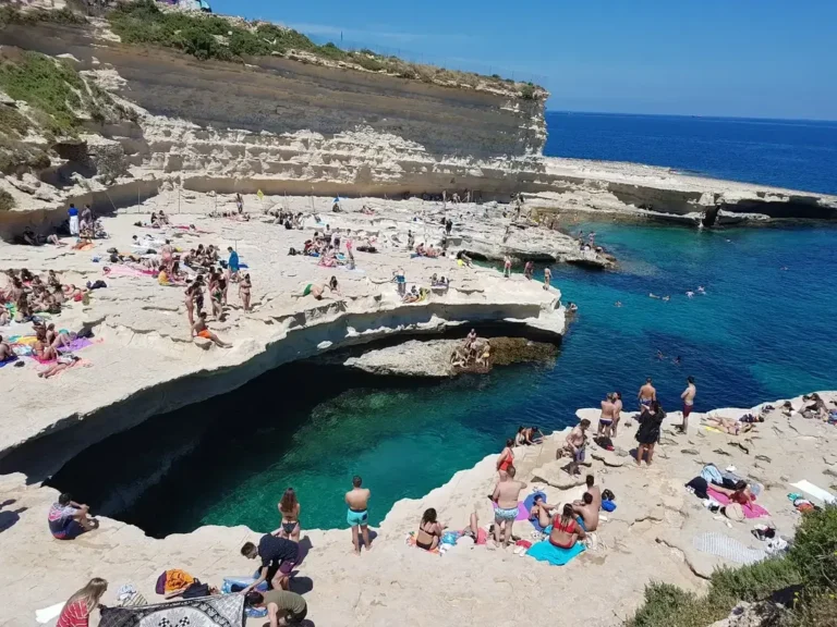 Crowded summer day at St Peter's Pool Malta with swimmers and sunbathers around the natural rock pool